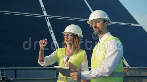 两名太阳能专家在太阳能电池板附近边聊边指着工地绿色能源概念视频的预览图