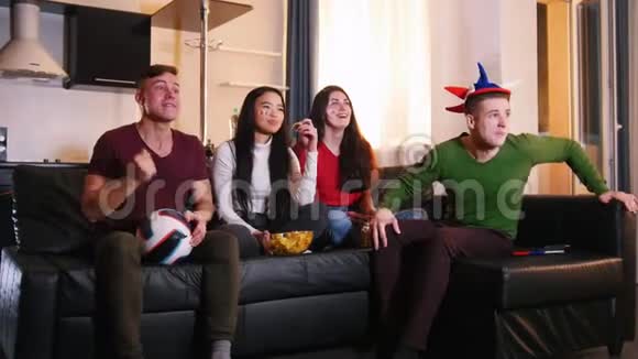 四个年轻的朋友坐在沙发上看足球赛一支球队射门一对夫妇很高兴视频的预览图