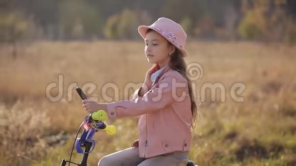 戴帽子的漂亮小女孩在自行车方向盘上的镜子里欣赏自己温暖柔和的光线视频的预览图