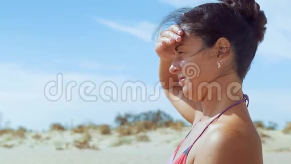 特写镜头穿着泳衣的美女坐在沙滩上闭上手眺望太阳视频的预览图