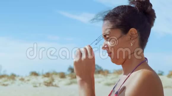 特写穿着泳装的美女坐在沙滩上戴着太阳镜视频的预览图