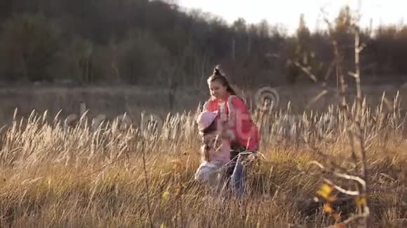 两个快乐的姐妹在田野的中央在温暖的夕阳的照耀下在草地上旋转视频的预览图