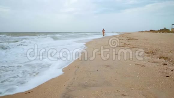 暴风雨中穿着白色泳衣的美丽女子在海边的水上奔跑视频的预览图