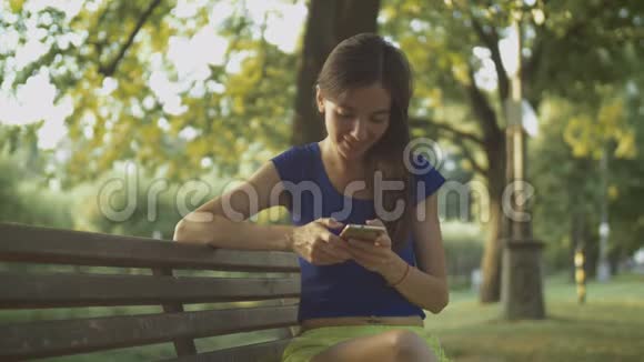 公园里微笑着的美女在手机上发短信视频的预览图