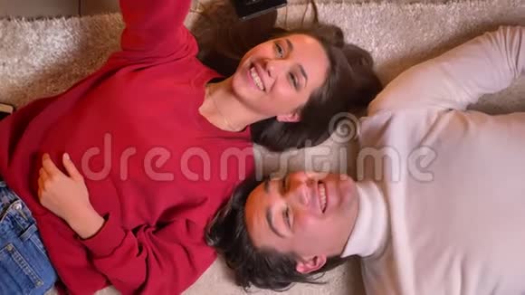 一对年轻漂亮的夫妇头对头躺在地毯上用智能手机在舒适的环境中制作自拍照片视频的预览图