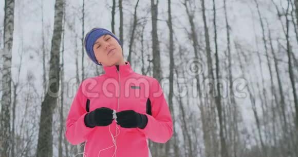 晨冬慢跑前的女孩把耳机插在耳朵里准备穿过自然公园视频的预览图