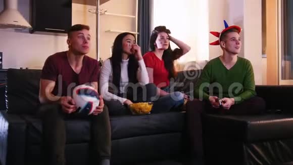 四个年轻人坐在沙发上看足球比赛一支球队进球了一对夫妇很高兴视频的预览图