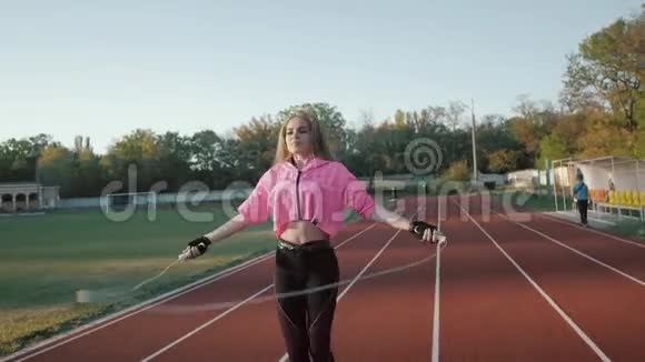 阳光明媚的早晨在体育场跑道上跳绳的年轻女子视频的预览图