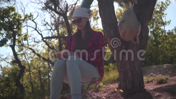 一个黑发红黑衬衫头巾和眼镜的女孩坐在森林里在电话里拍照视频的预览图