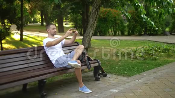 全速射击一位男性博主坐在公园长凳上使用智能手机他和某人有个视频通话视频的预览图