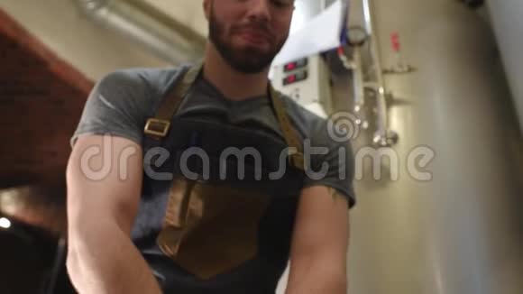 一个长胡子的年轻人穿着围裙在啤酒厂工作手里拿着麦芽手里拿着金属啤酒罐视频的预览图