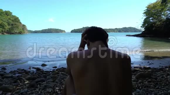 在海边的麻烦人年轻人坐在海滩上看上去很担心他抓住了他的头视频的预览图