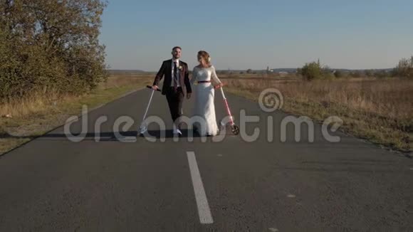 美丽的新婚夫妇手里拿着一辆摩托车正沿着金色的秋天的道路走着视频的预览图