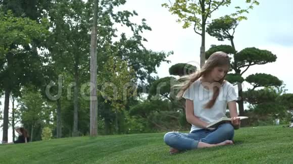 公园里年轻漂亮的女孩正在看书一个学生正在翻阅一本书坐在草地上视频的预览图