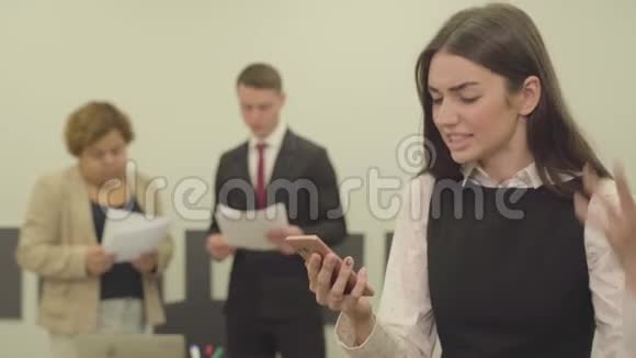身着正装的愤怒年轻女子的画像在办公室的前台用手机讲话而她的男性和视频的预览图