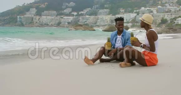 在海滩上喝菠萝汁的非裔美国人夫妇的侧面景色视频的预览图