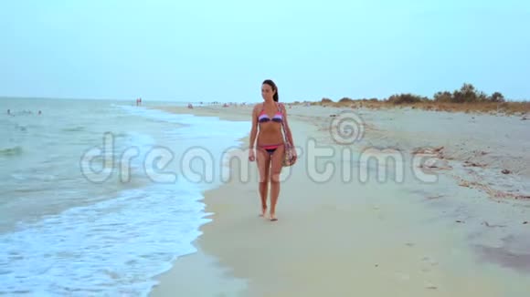 穿着条纹泳装的美丽黝黑女人在海边漫步视频的预览图
