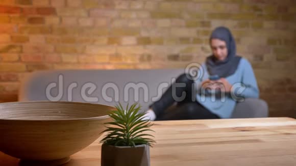 年轻迷人的穆斯林女性戴着头巾躺在室内沙发上休息时用手机拍摄特写镜头视频的预览图
