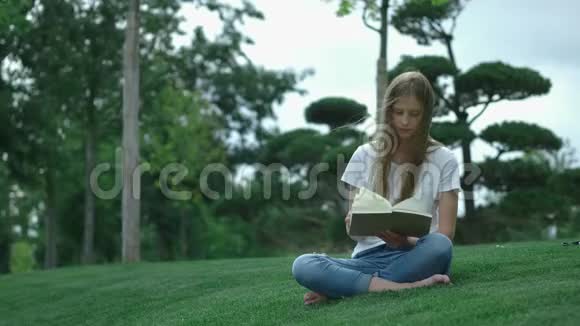 公园里年轻漂亮的女孩正在看书一个学生正在翻阅一本书坐在草地上视频的预览图