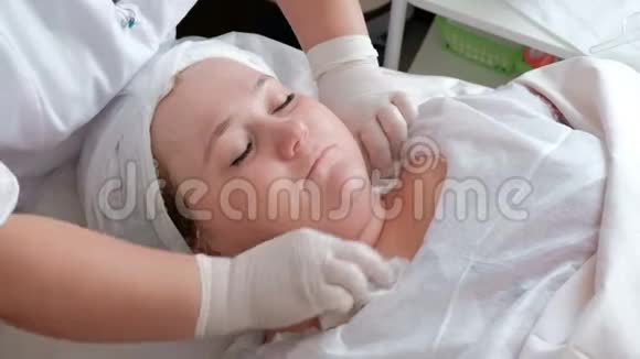 戴着白手套的美容师擦着一个丰满女人的脸和脖子美容护肤女性美容术视频的预览图