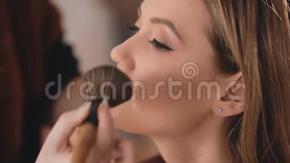 化妆师在一个白人金发模特的脸上用专业刷子涂粉完成化妆视频的预览图