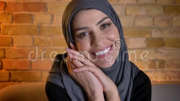 在舒适的公寓里戴着头巾看着摄像机微笑着的穆斯林成年女性特写照片视频的预览图
