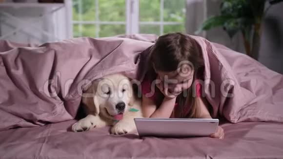 小女孩和小狗在床上看动画片视频的预览图