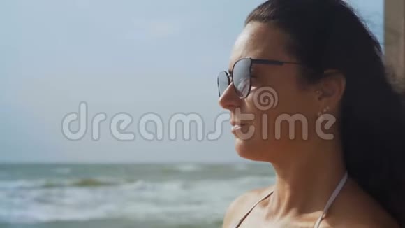 穿着白色泳衣和太阳镜的美女坐在海边的鸡尾酒视频的预览图