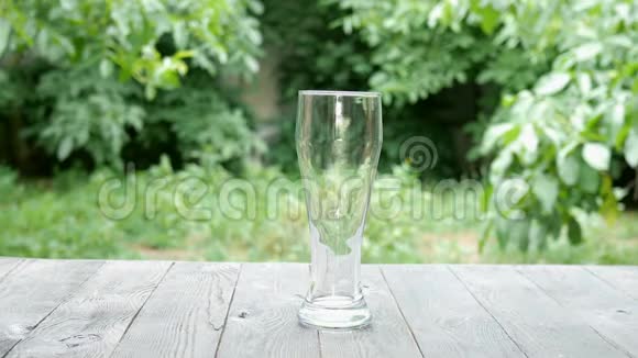 在木桌上的夏季花园里从一瓶深色玻璃中将淡啤酒倒入高玻璃中视频的预览图