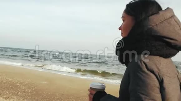 女孩沿着大海走手里拿着一个一次性杯子和一杯饮料视频的预览图