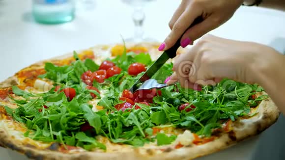 特写大的多汁热的比萨饼与绿色木耳和樱桃番茄女人用刀叉切披萨视频的预览图