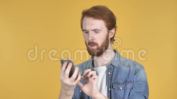 红发人在使用智能手机时为成功而兴奋黄色背景视频的预览图