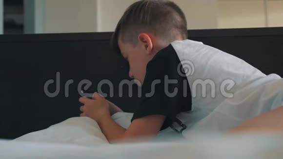 一个有智能手机的男孩躺在床上男孩借助智能手机与朋友交流视频的预览图