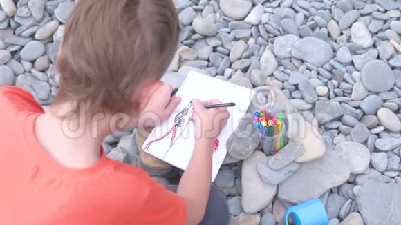 男孩坐在海边的石滩上画着记号后景视频的预览图