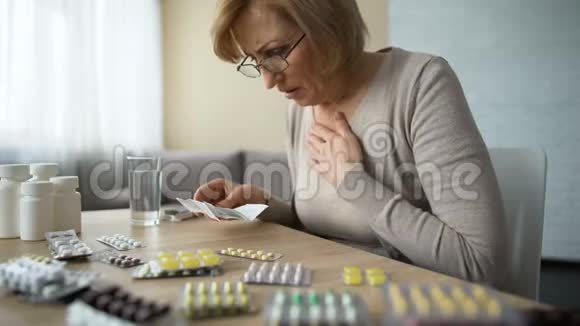 悲伤的女人看着满桌的药丸和叹息老年疾病成瘾视频的预览图