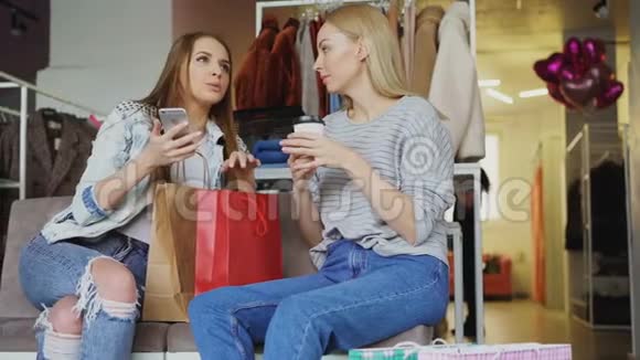 漂亮的女孩坐在女式服装店他们喝着咖啡漫不经心地聊天用着视频的预览图