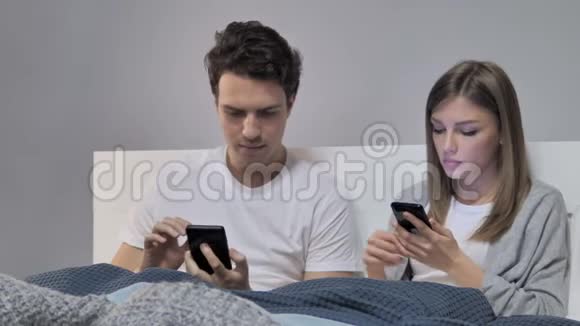 年轻夫妇在床上使用智能手机分享信息视频的预览图