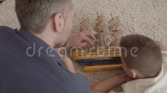 父亲和儿子躺在地板上的毛茸茸的地毯上玩船模特写家庭开支视频的预览图