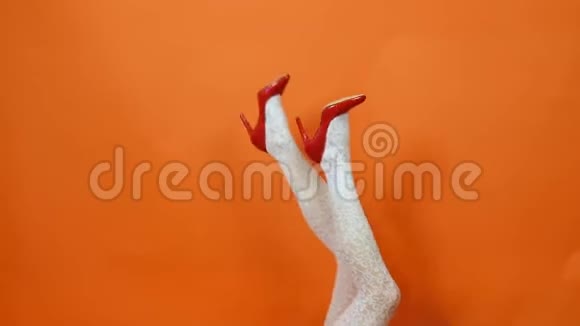 性感的女性腿在红色高跟鞋和鱼网丝袜摆在橙色背景在工作室复古风格视频的预览图