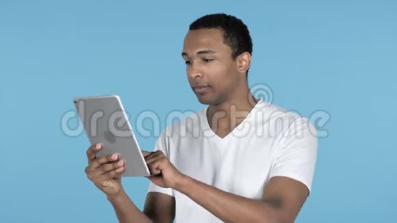 在使用平板电脑时失去非洲青年男子的震惊蓝色背景视频的预览图