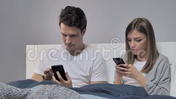 年轻夫妇在床上放松时使用智能手机视频的预览图