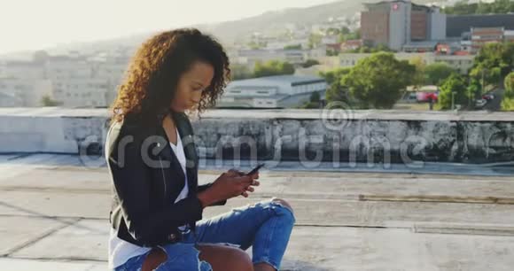 城市屋顶上使用智能手机的时尚年轻女性视频的预览图