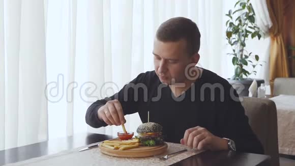 一个年轻人坐在咖啡馆里吃一份开胃的炸薯条旁边是一个大汉堡摊在桌子上视频的预览图