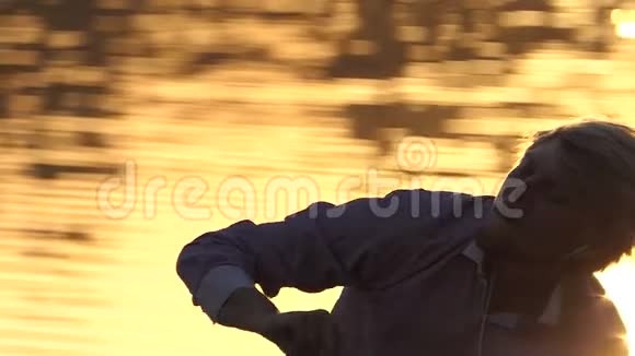 在斯洛莫日落时分一个滑稽的男人在湖边听音乐视频的预览图