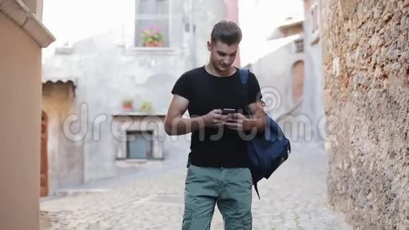 穿着黑色T恤背着背包在老城区行走使用智能手机的英俊青年视频的预览图