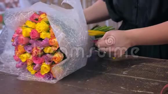 女花店在花店用纸包装玫瑰花束手特写视频的预览图