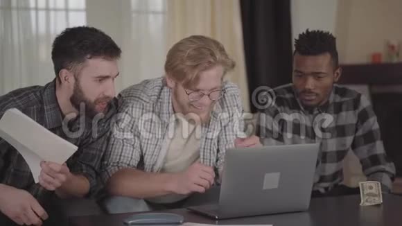 两个白种人和一个非裔美国人坐在笔记本电脑前在家休息多元文化公司视频的预览图