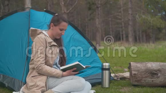 一个留着长发的小女孩正坐在森林里的一个蓝色帐篷附近看书视频的预览图