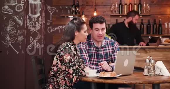 白种人夫妇看着笔记本电脑喝着带羊角面包的咖啡视频的预览图
