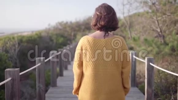 葡萄牙海岸线上一个穿着黄色夹克的女人走在一条木制的人行道上被大自然包围着视频的预览图